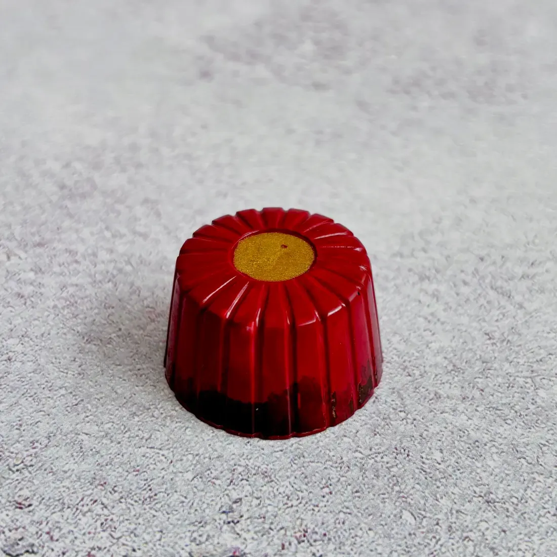Fior di Fragola — single red flower praline with ridged petals and gold dusted center, three-quarter angle on grey marble