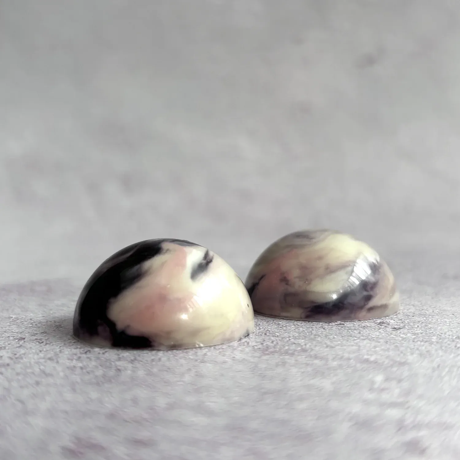 Ibisco — two dome-shaped white chocolate pralines with marbled pink, purple and black swirl decoration on marble